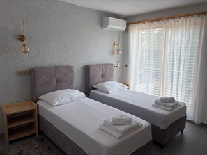 Et hotelværelse med to senge, et trænatbord, en pelsrug og et vindue med lette gardiner.