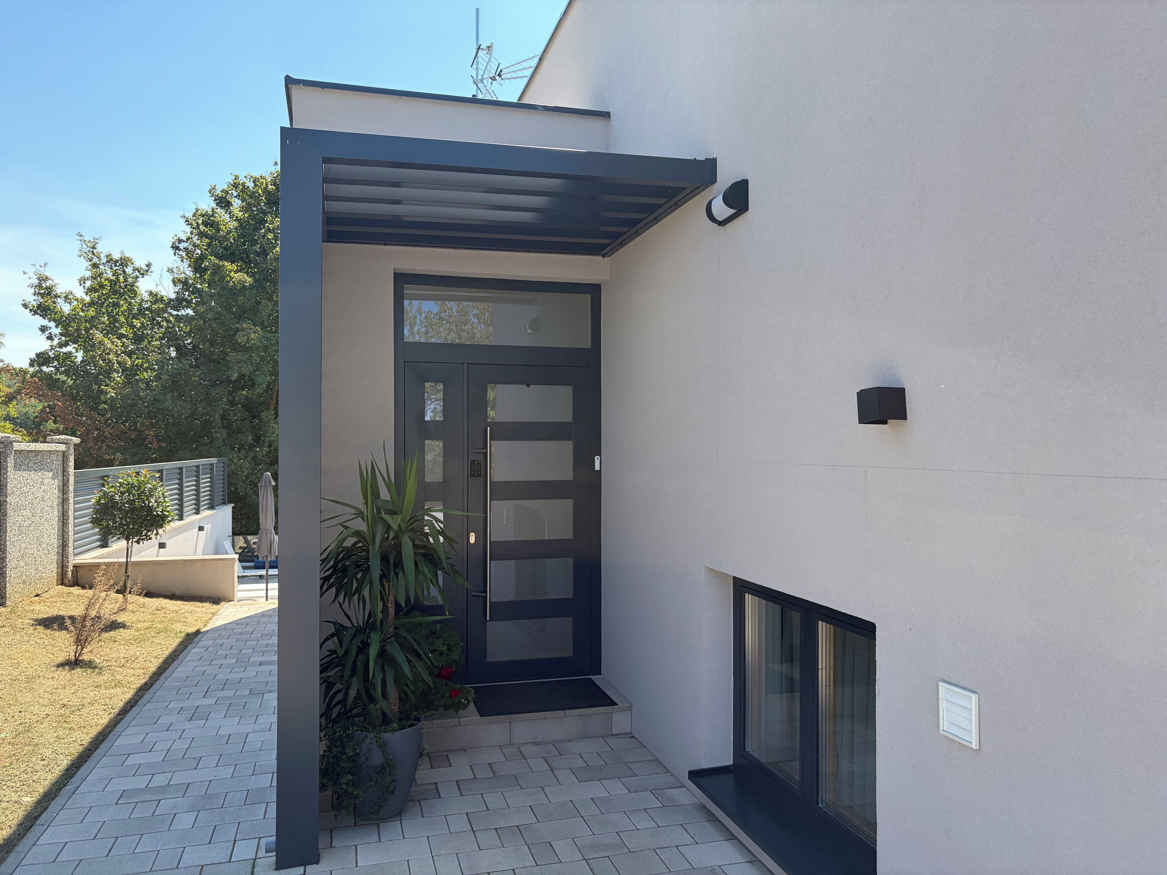 A modern building entrance with a dark door, a small outdoor seating area, and a potted plant.