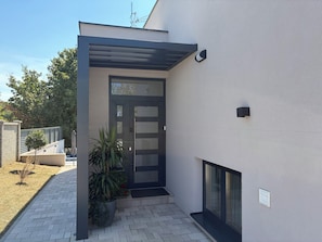 A modern building entrance with a dark door, a small outdoor seating area, and a potted plant.