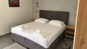 Una cama bien hecha con almohadas y toallas dobladas, cabecera, mesitas de noche y un cuadro en la pared.