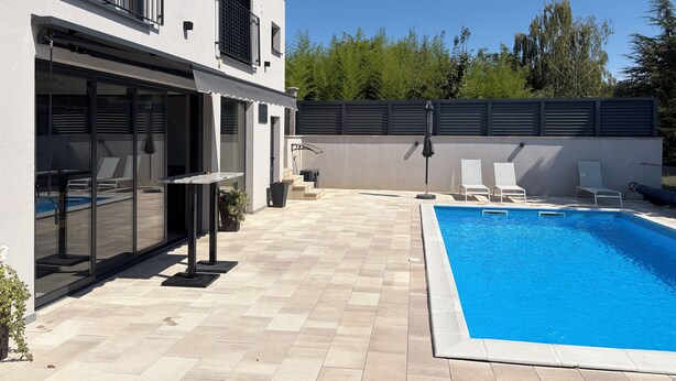 Una casa moderna con piscina, puertas de cristal y mobiliario exterior.