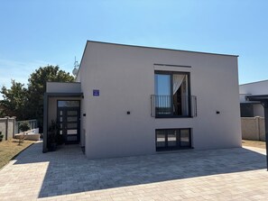 Un edificio moderno con fachada plana, un balcón con barandilla negra y una puerta con ventanal.