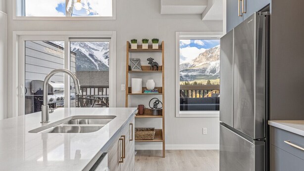 Una cocina moderna con un refrigerador de acero inoxidable, una repisa de madera con objetos decorativos y vistas a montañas a través de amplias ventanas.