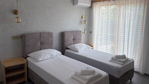 Ein Hotelzimmer mit zwei Betten, einem Holznachttisch, einem Fellteppich und einem Fenster mit durchsichtigen Vorhängen.