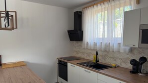 Eine kompakte Küche mit Holzarbeitsplatte, integriertem Geschirrspüler, Spüle mit Armatur und Fenster mit transparenten Vorhängen.