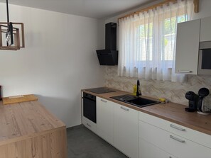 A compact kitchen with a wooden countertop, a built-in dishwasher, a sink with a faucet, and a window with sheer curtains. - Modern villa with pool, jacuzzi, and sauna in Bilogora for relaxing getaway. (Maglenča)