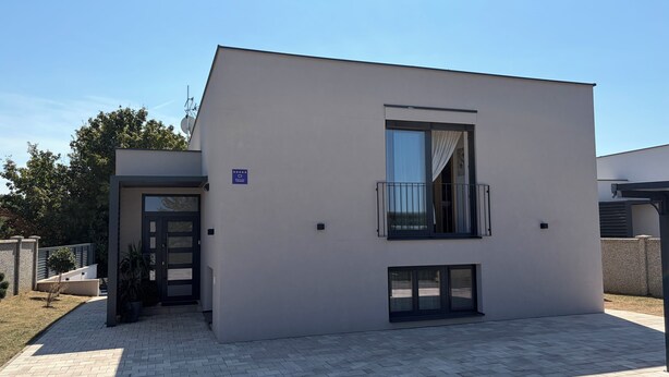 Ein modernes Gebäude mit flacher Fassade, einem Balkon mit schwarzem Geländer und einer Tür mit Fenster.