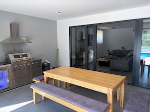 A modern kitchen with a built-in oven and a dining area with a wooden table and benches. - Modern villa with pool, jacuzzi, and sauna in Bilogora for relaxing getaway. (Maglenča)