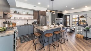 Eine moderne Küche mit einer zentralen Kochinsel, Barhocker und einem Essbereich mit Sofa und Couchtisch.