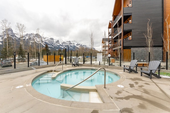Ein Poolbereich mit Blick auf schneebedeckte Berge, umgeben von einem Gebäude mit Balkonen und einer Holzterrasse.