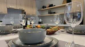 A modern kitchen with wooden cabinets, a dining table set with plates, bowls, and wine glasses. - Alpine Ascent - Pool, Hot Tub & Fitness - Parking (Canmore)