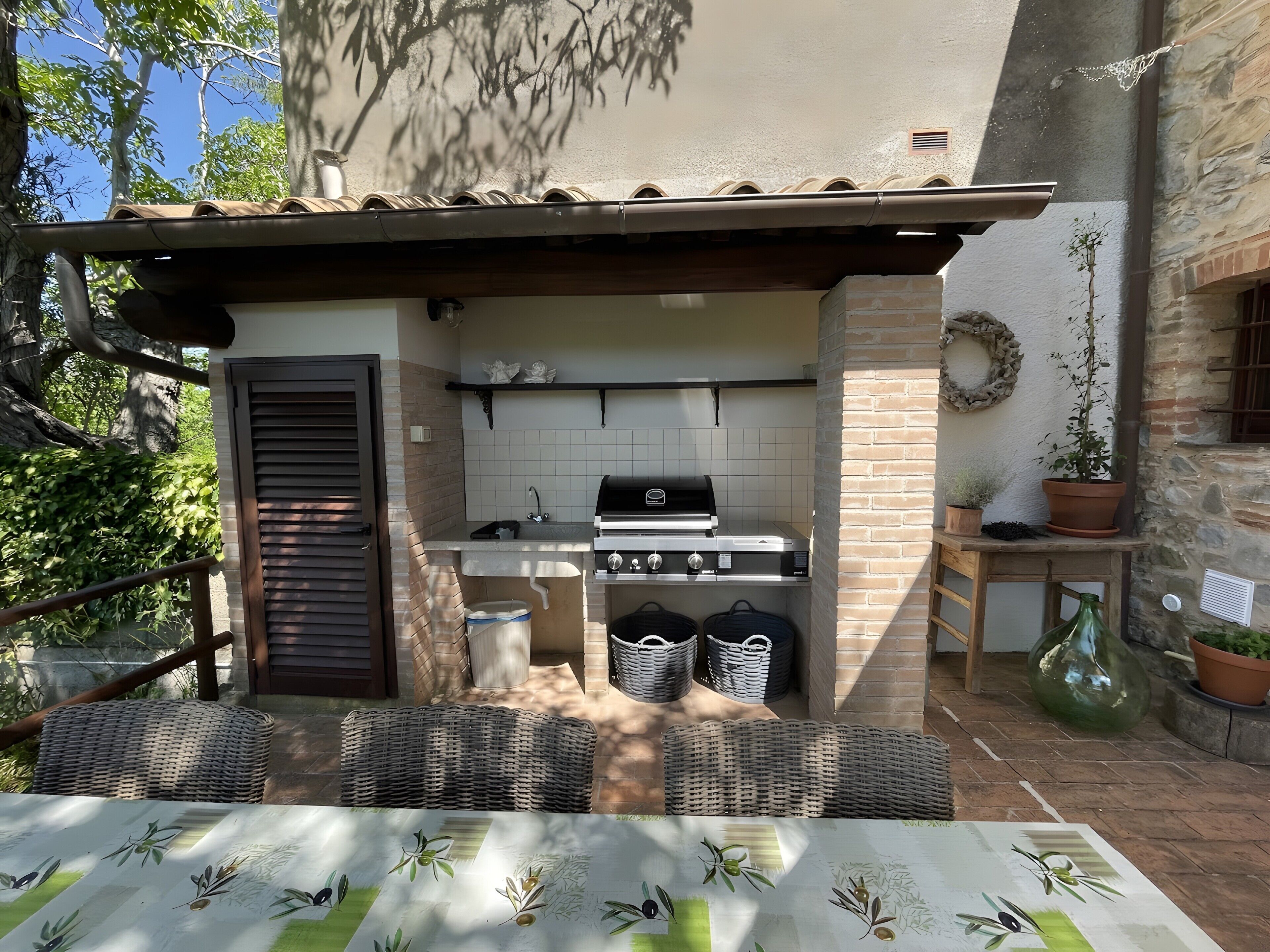 An outdoor kitchen with a grill, wicker furniture, and potted plants.