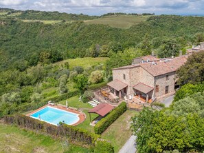Eine Steinvilla mit Swimmingpool, umgeben von üppiger Vegetation und Hügeln.
