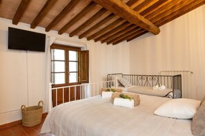 Ein Schlafzimmer mit zwei Betten, einer Holzbalkendecke, einem an der Wand montierten Fernseher und einem Fenster mit Vorhängen.