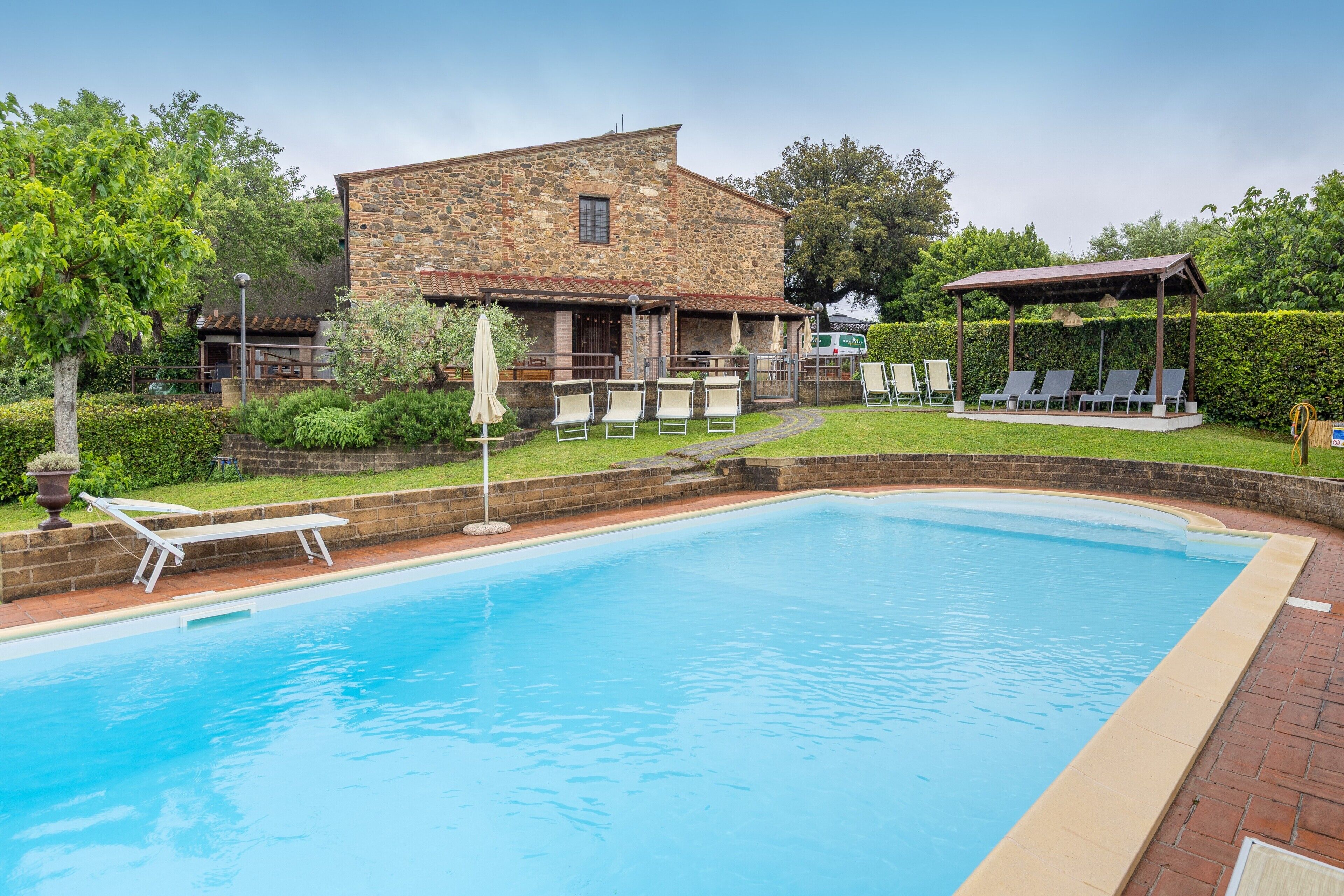 Una piscina con tumbonas, un edificio de piedra y una zona de estar techada.