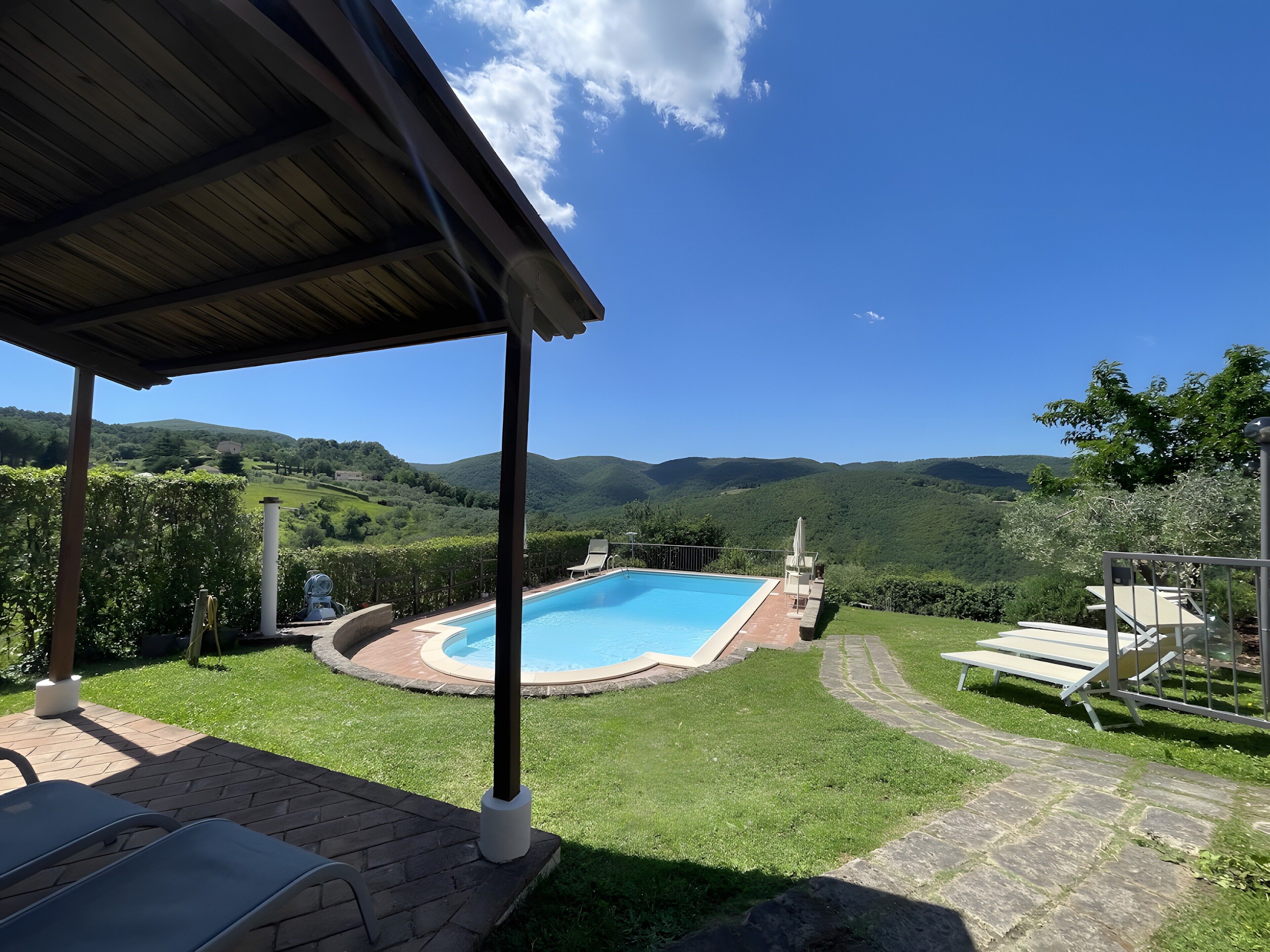 Une piscine avec vue sur des collines verdoyantes, un patio couvert et un chemin en pierre.