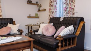 Ein Wohnzimmer mit einer schwarzen Ledersofa, einem Holztisch und blumigen Vorhängen.