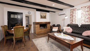 Ein Wohnzimmer mit Kamin, einer Couch, einem Esstisch mit Stühlen und einer Wanduhr.