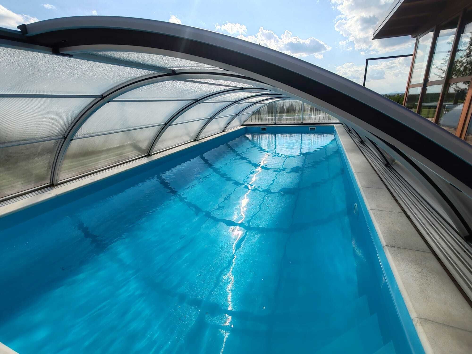 Une piscine dotée d’une structure de toit incurvée, d’une eau d’un bleu limpide et offrant une vue sur le ciel.
