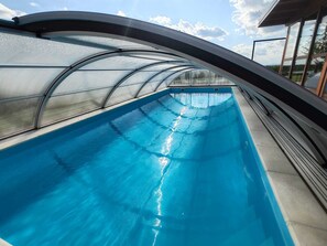 A swimming pool with a curved roof structure, clear blue water, and a view of the sky.