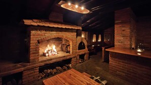 A rustic brick fireplace with a fire, wooden benches, and a stone wall.