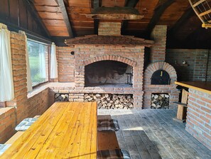 A rustic outdoor kitchen with a brick oven, wooden table, and seating area.