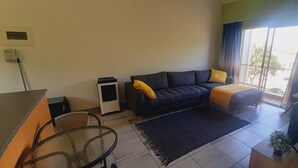 A modern living room with a dark sofa, a glass table, and a large window with curtains.