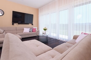 Uma sala de estar com sofá, mesa de centro, televisão de tela plana e cortinas leves.