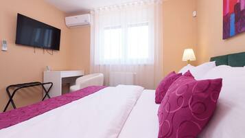 Une chambre d’hôtel avec un lit, un bureau, une chaise, une télévision et une fenêtre avec des rideaux.