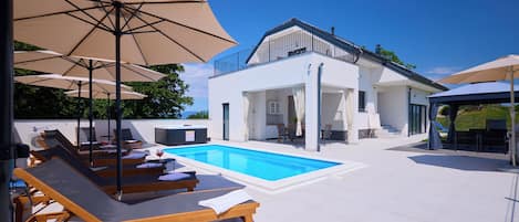 A poolside area with lounge chairs and umbrellas, a pool, and a two-story building with a balcony.