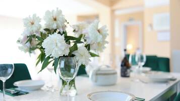 Une table à manger dressée avec de l’assiette blanche, des verres à vin transparents et un vase rempli de fleurs blanches.