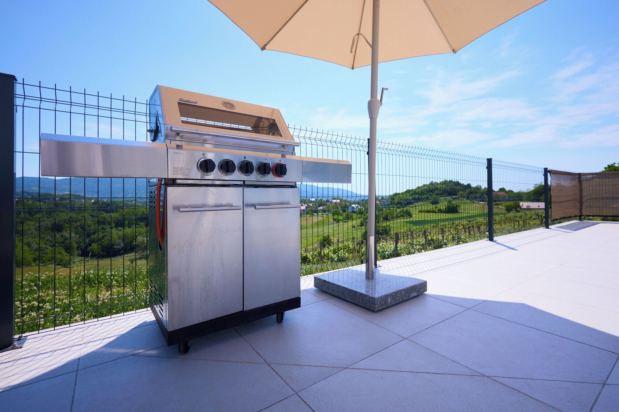 Un barbecue d’extérieur en acier inoxydable, doté de quatre brûleurs, d’un panneau de commande et d’un four intégré, installé sur une terrasse offrant une vue sur un paysage verdoyant.