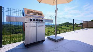 Un barbecue d’extérieur en acier inoxydable, doté de quatre brûleurs, d’un panneau de commande et d’un four intégré, installé sur une terrasse offrant une vue sur un paysage verdoyant.
