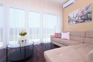 A modern living room with a beige sofa, a glass coffee table, and a painting of the Eiffel Tower on the wall.