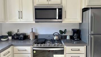 A modern kitchen with white cabinets, a stainless steel microwave, a gas stove, and a refrigerator.