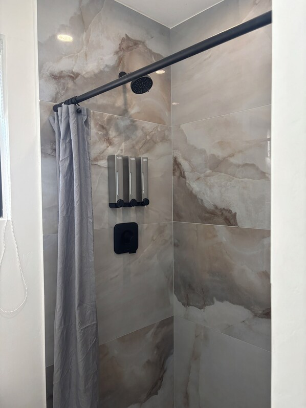 Un área de ducha con pared de mármol, un cabezal de ducha y un perchero para toallas.