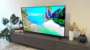Un televisor de pantalla plana sobre un mueble de madera mostrando una playa pintoresca con acantilados.