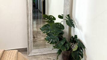Una habitación con un espejo grande, una planta de monstera en maceta y una cama color beige.