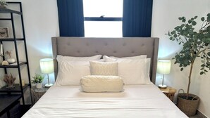 Una cama bien hecha con ropa de cama blanca, cabecera capitonada y lámpara de noche.