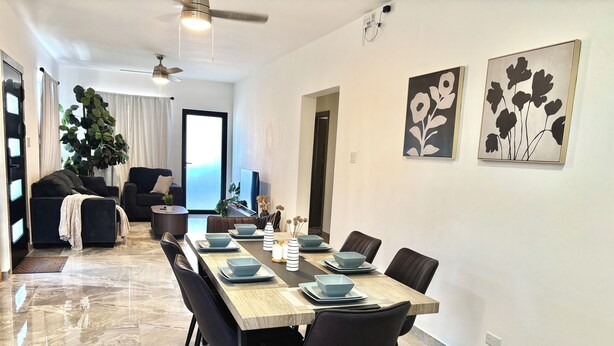 Un comedor moderno con una mesa de madera para seis personas, sillas negras y una gran planta en maceta al fondo.