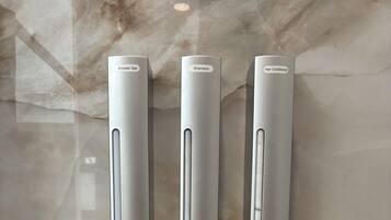 Dispensador montado en la pared con tres compartimentos etiquetados para gel de ducha, champú y acondicionador para cabello.