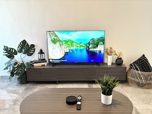 Un téléviseur à écran plat posé sur un meuble TV en bois foncé, avec une télécommande et une plante en pot sur une table basse ronde en bois.