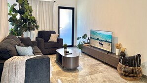 Una sala de estar moderna con un sofá, un sillón, una mesa de centro y un televisor que muestra una escena de naturaleza.