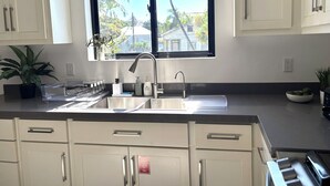 Una cocina con un amplio ventanal, armarios blancos y un lavamanos de acero inoxidable.