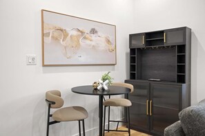 A modern room with a round table, two chairs, a dark wood cabinet with gold handles, and a large abstract painting on the wall. - 6BD/5BA of Modern Elegance | Cinema, Games, HotTub (Dallas)