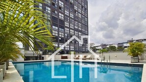 A swimming pool with lounge chairs and palm trees, surrounded by a high-rise building. - Cali - Edificio Miro Living Refugio (Cali)