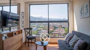 A modern living room with a large window, a flat-screen TV, a sofa, and a small table. - Cali - Edificio Miro Living Refugio (Cali)