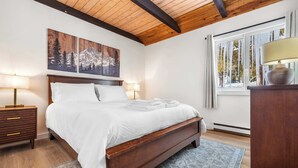 Una camera da letto con un letto in legno, due comodini con lampade, un'ampia finestra vista alberi e un quadro appeso al muro.