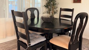 Un comedor con una mesa redonda, cuatro sillas, un ventilador de techo, una planta en maceta y un cuadro en la pared.