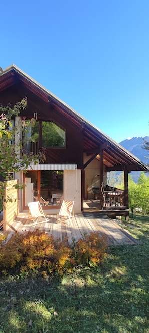 Une maison en bois avec une terrasse, deux chaises et une table.